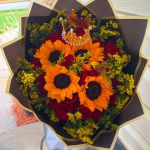 Bouquet of 4 sunflowers and 16 red roses with a decorative crown and black wrapping with gold trim.