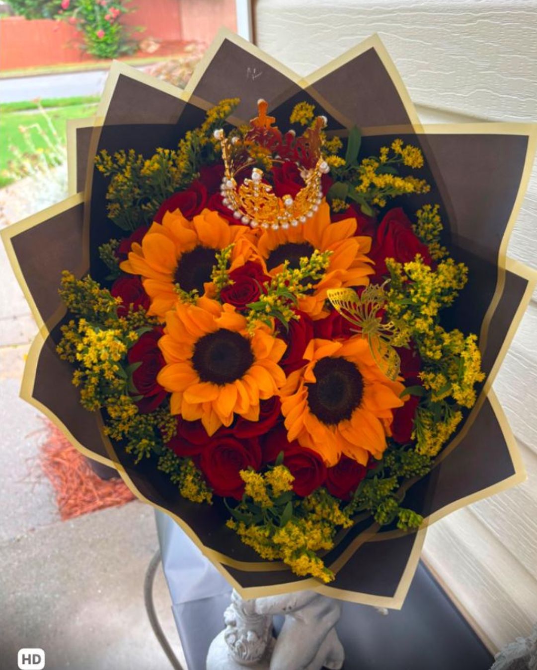 Bouquet of 4 sunflowers and 16 red roses with a decorative crown and black wrapping with gold trim.