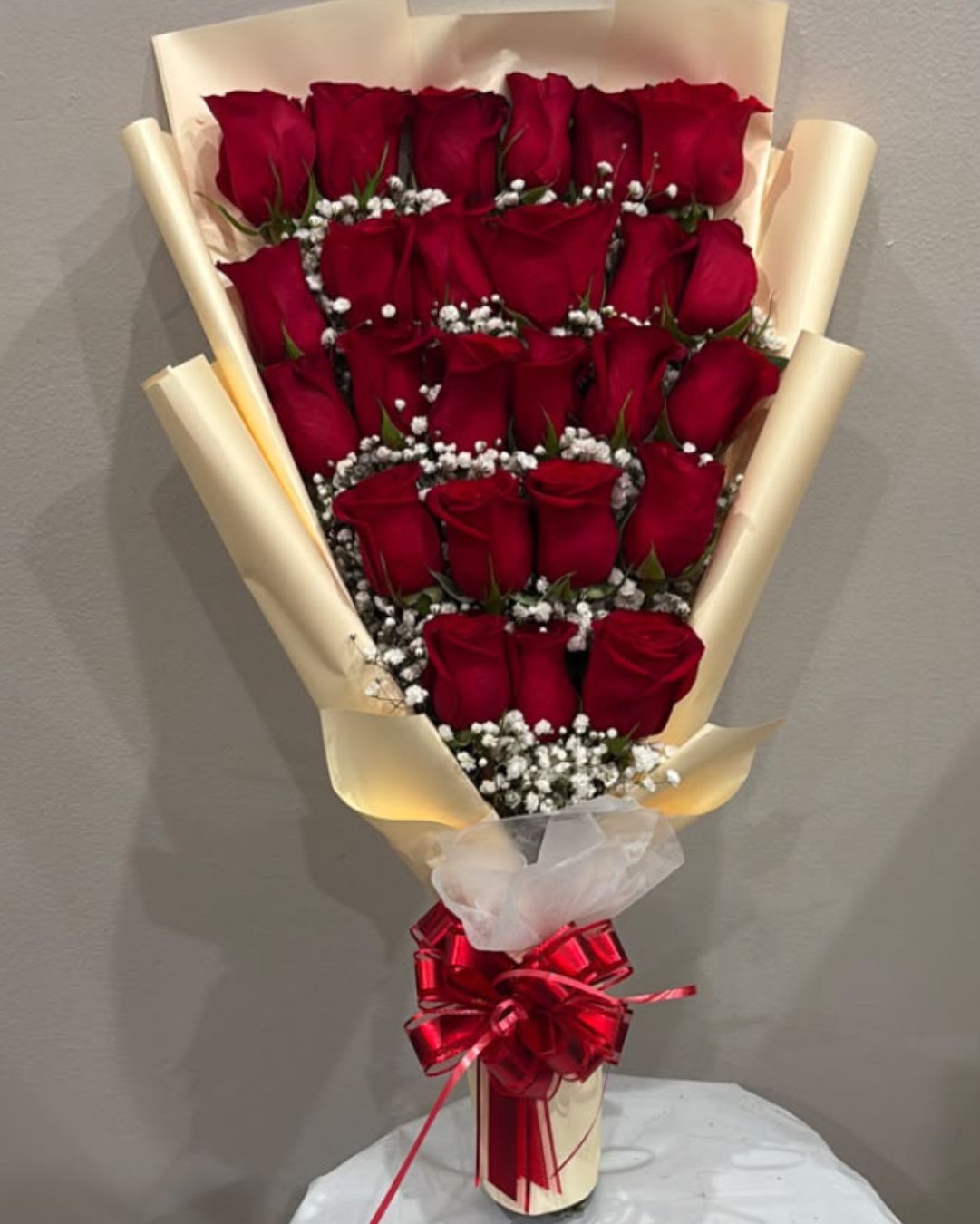 Baby Bouquet of 25 red roses with white filler flowers, gold-toned wrapping, and a red bow.