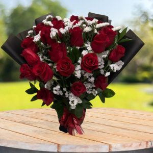 Happy Bouquet of 20 red roses with white statice, Israeli ruscus greenery, black wrapping, and a red bow.