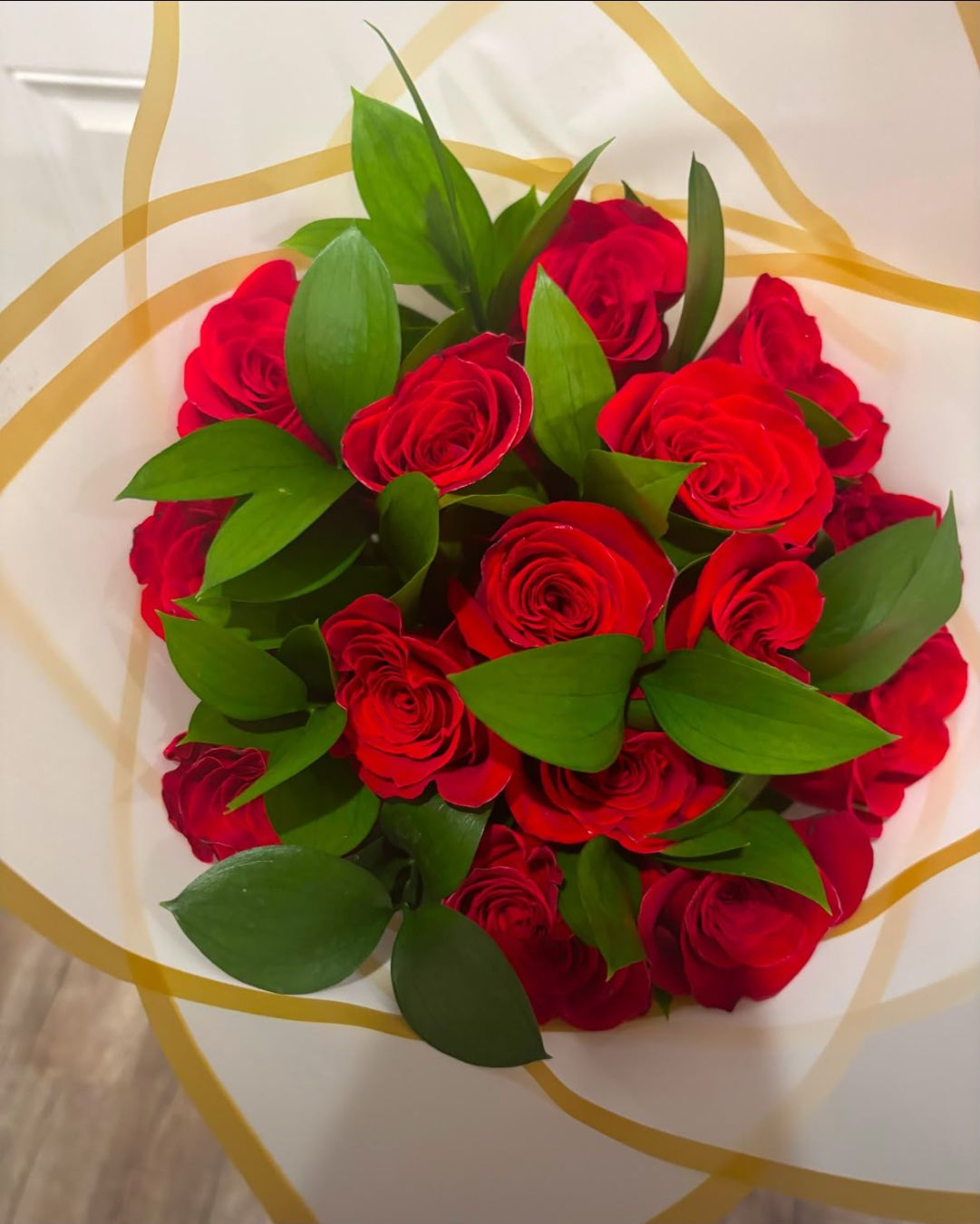 Ruscus Bouquet of 18 red roses with green foliage and white wrapping with gold trim.